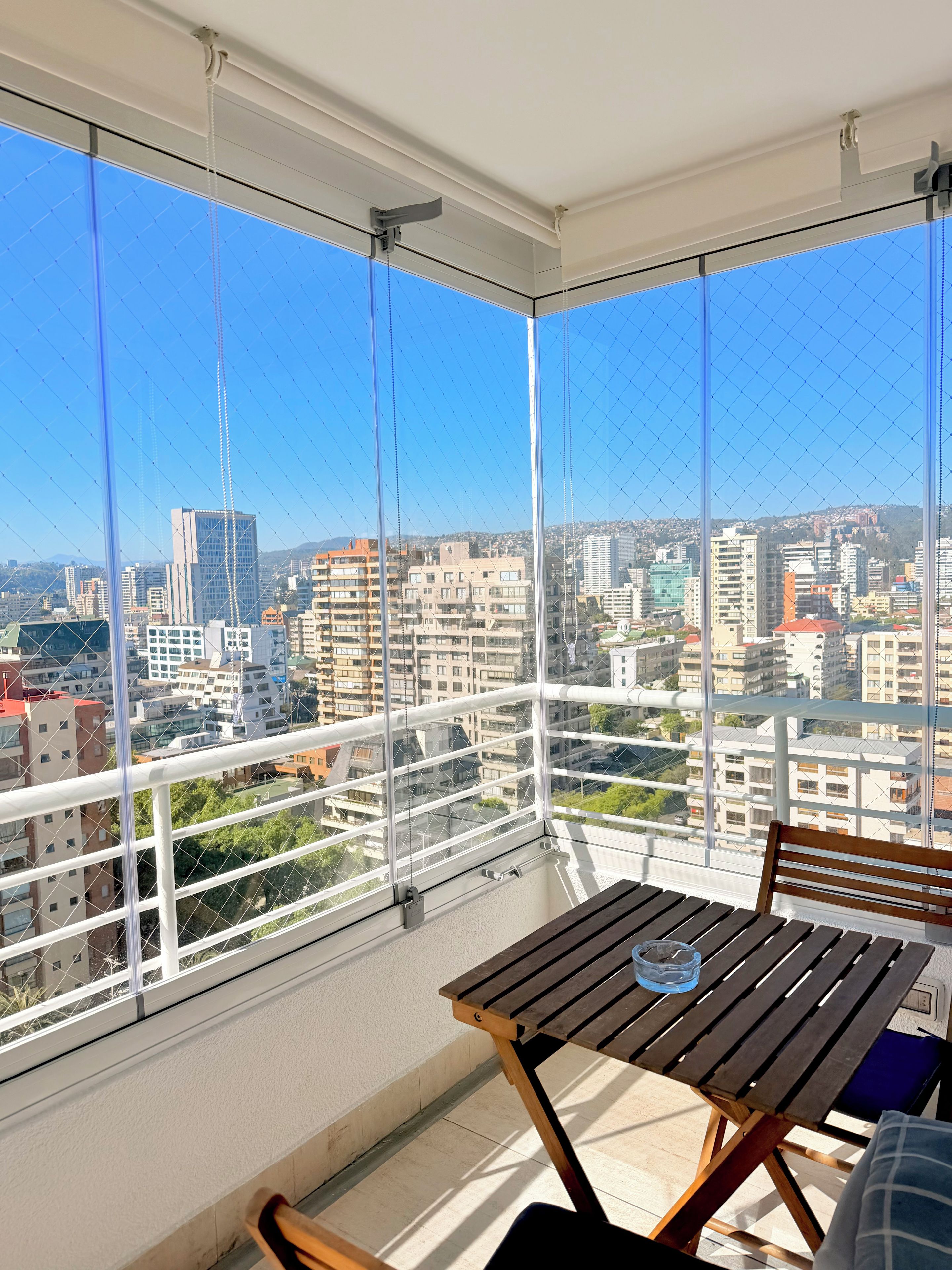 Un balcon avec une table et des chaises, donnant sur un paysage urbain avec des bâtiments et un ciel dégagé.