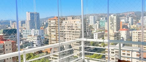 A balcony with a table and chairs, overlooking a cityscape with buildings and a clear sky.