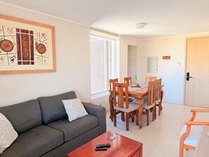 Ein Wohnzimmer mit einem grauen Sofa, einem Holzesstisch mit vier Stühlen und einem roten Couchtisch.