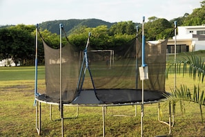 A trampoline with a safety net, set up in a grassy area with trees and a building in the background. - Casa Kyma Playa Herradura (Herradura)