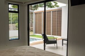 Un dormitorio con cama, una silla y vistas a una piscina y jardín a través de un ventanal corredizo.