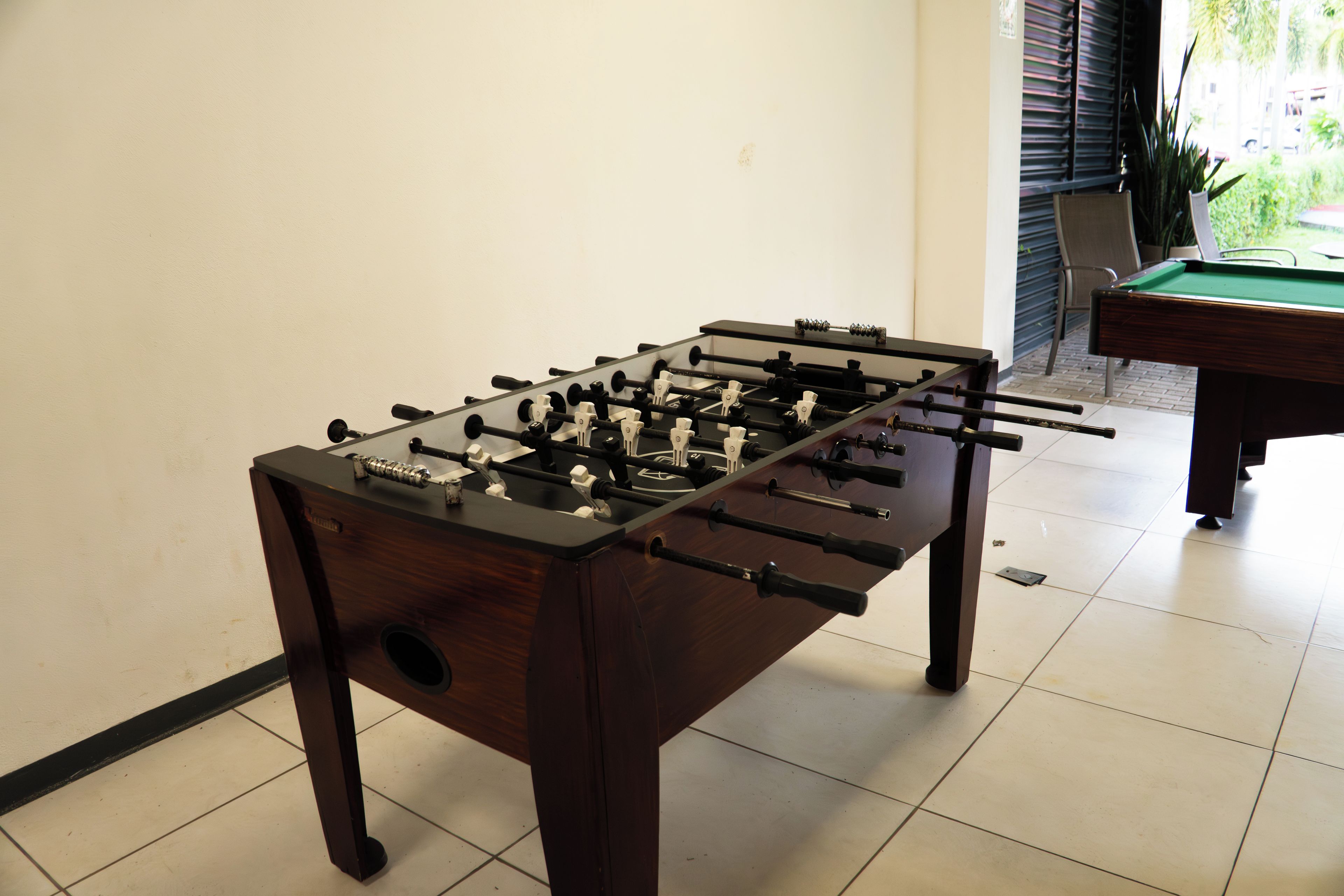 A foosball table in a room with a pool table and a chair in the background.