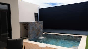 Una piscina amb cascada, envoltada per un pont de fusta i una zona d'estar exterior moderna.