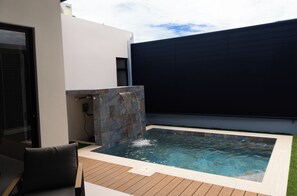 A swimming pool with a waterfall feature, surrounded by a wooden deck and a modern outdoor seating area. - Casa Kyma Playa Herradura (Herradura)