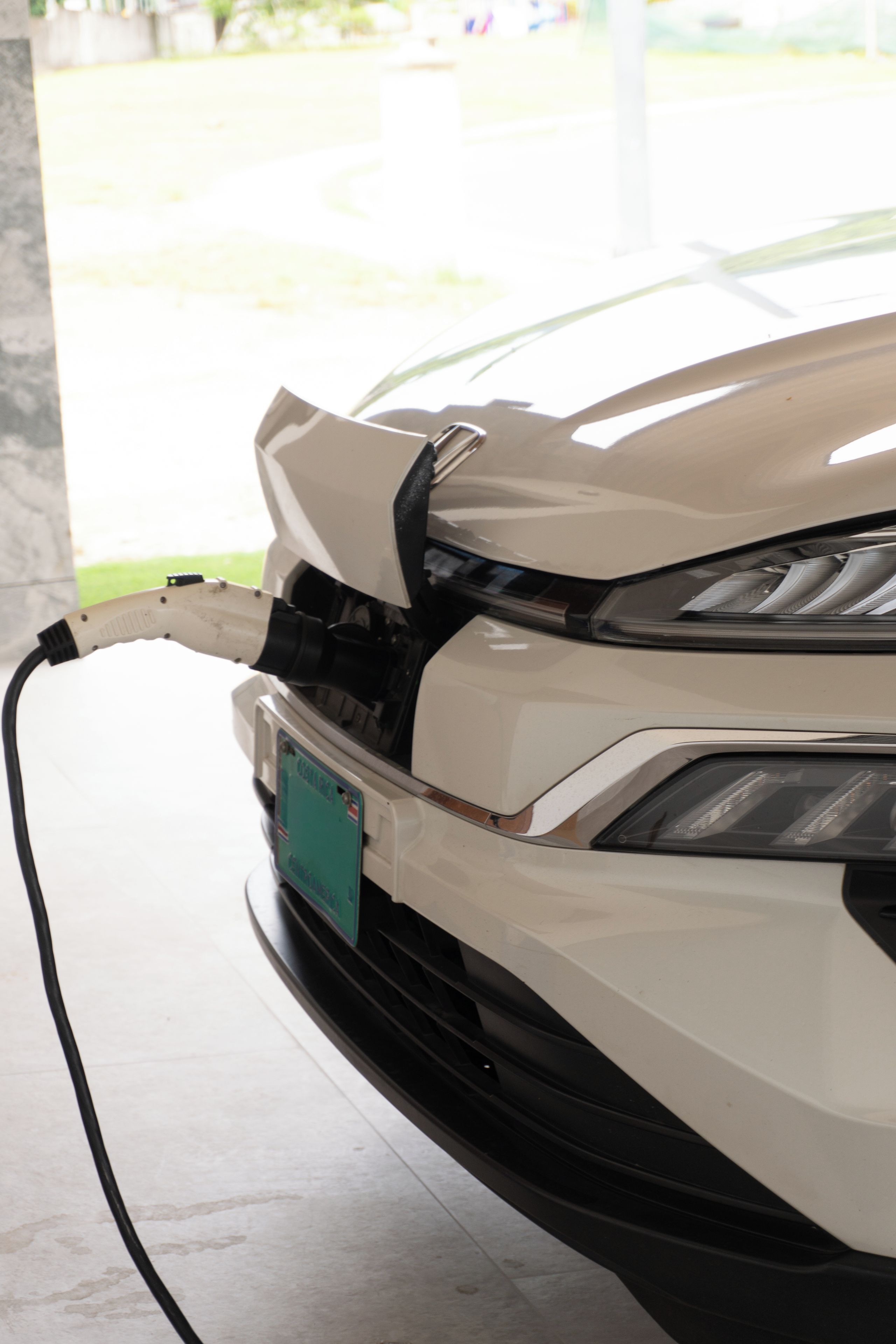 A white car with a damaged front bumper and a visible charging cable.
