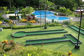 Zona de piscina con diseño curvo, rodeada de vegetación y un área de juegos infantiles.