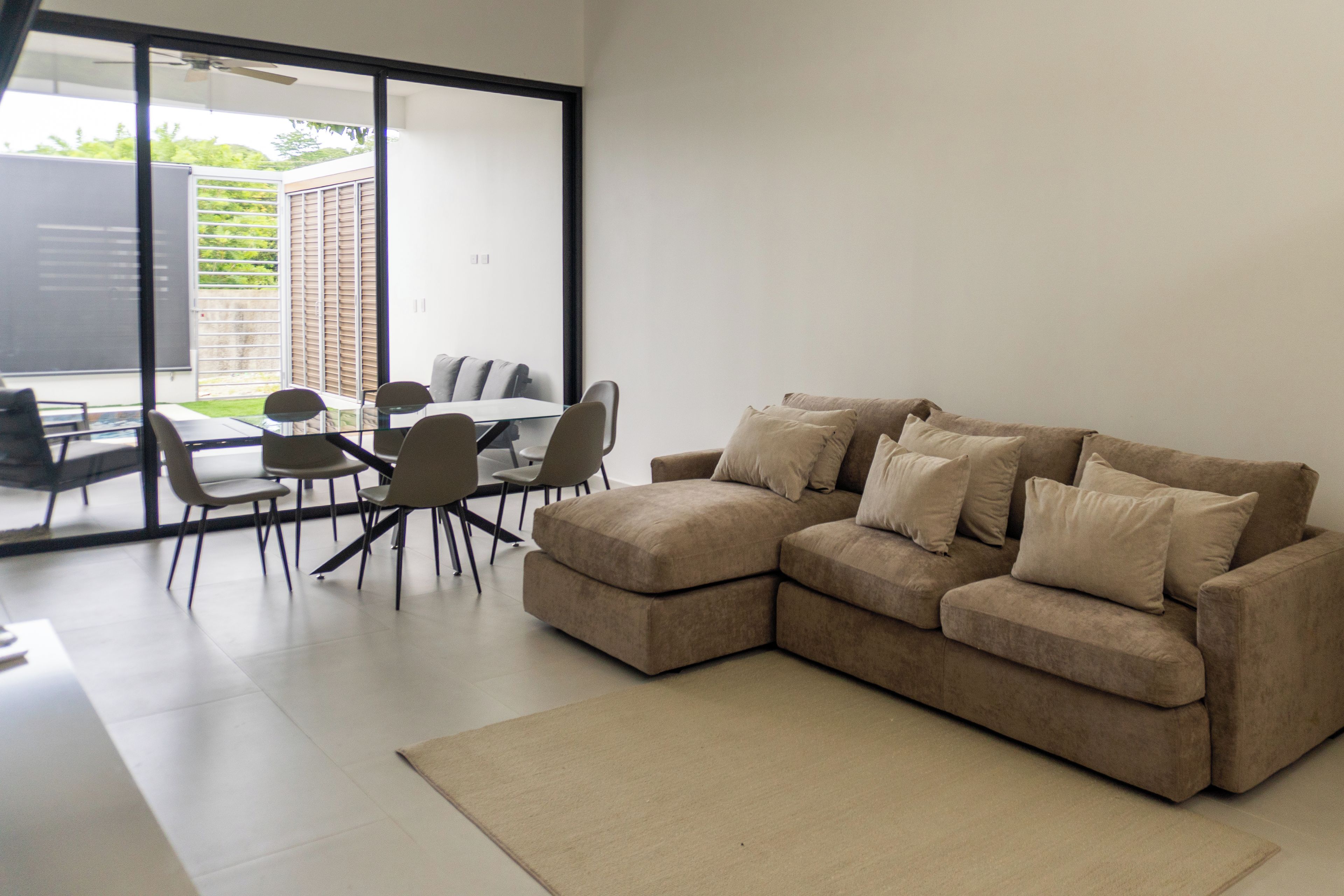A modern living room with a sectional sofa, a glass dining table, and chairs.