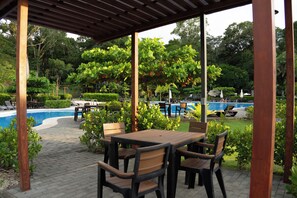 Un espacio de estar techado al aire libre con piscina al fondo.