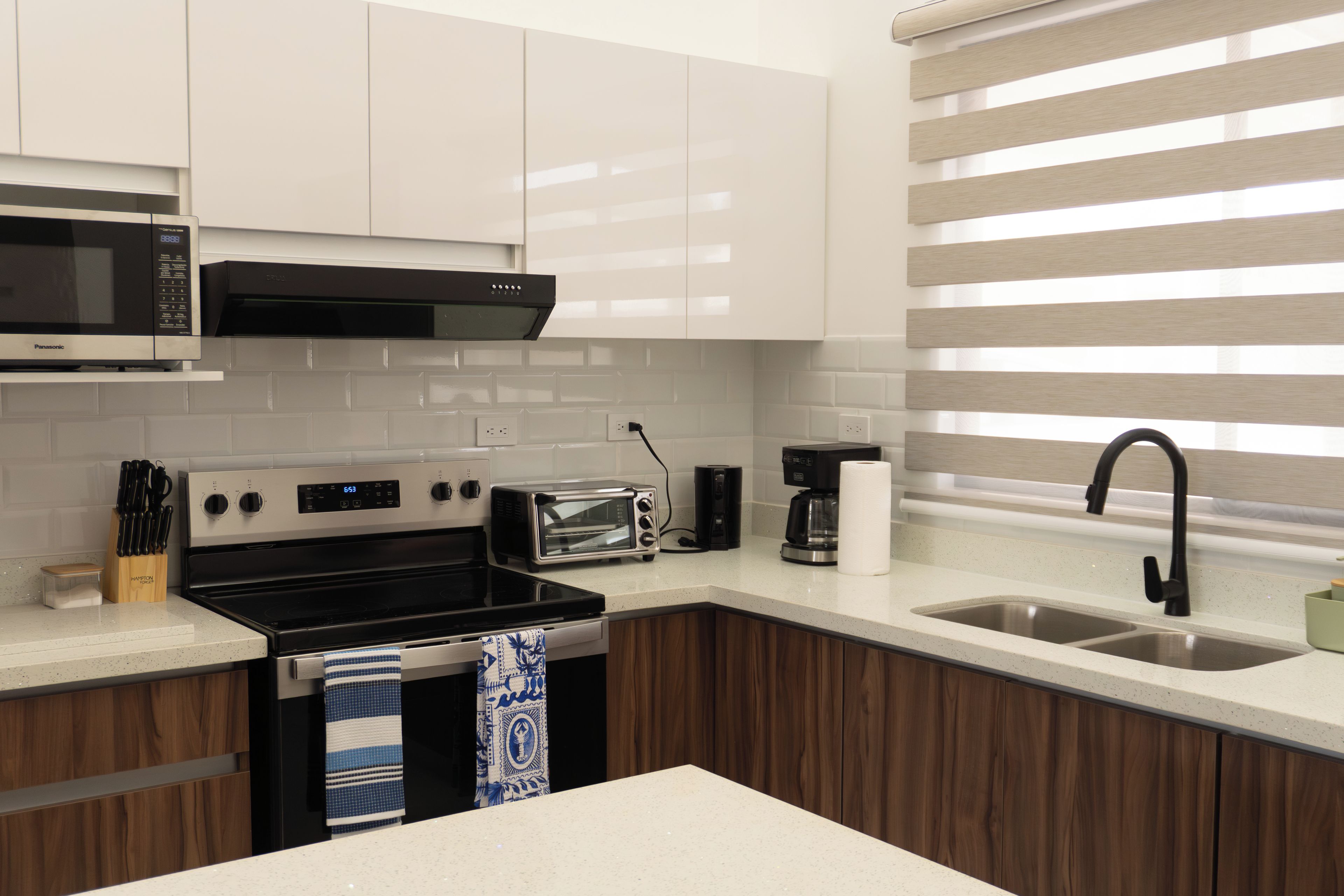 Une cuisine moderne avec des meubles blancs, un four à micro-ondes, une cuisinière, un grille-pain et un évier.