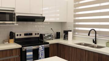 Une cuisine moderne avec des meubles blancs, un four à micro-ondes, une cuisinière, un grille-pain et un évier.