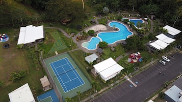 An aerial view of a resort with multiple swimming pools, tennis courts, and a parking area.