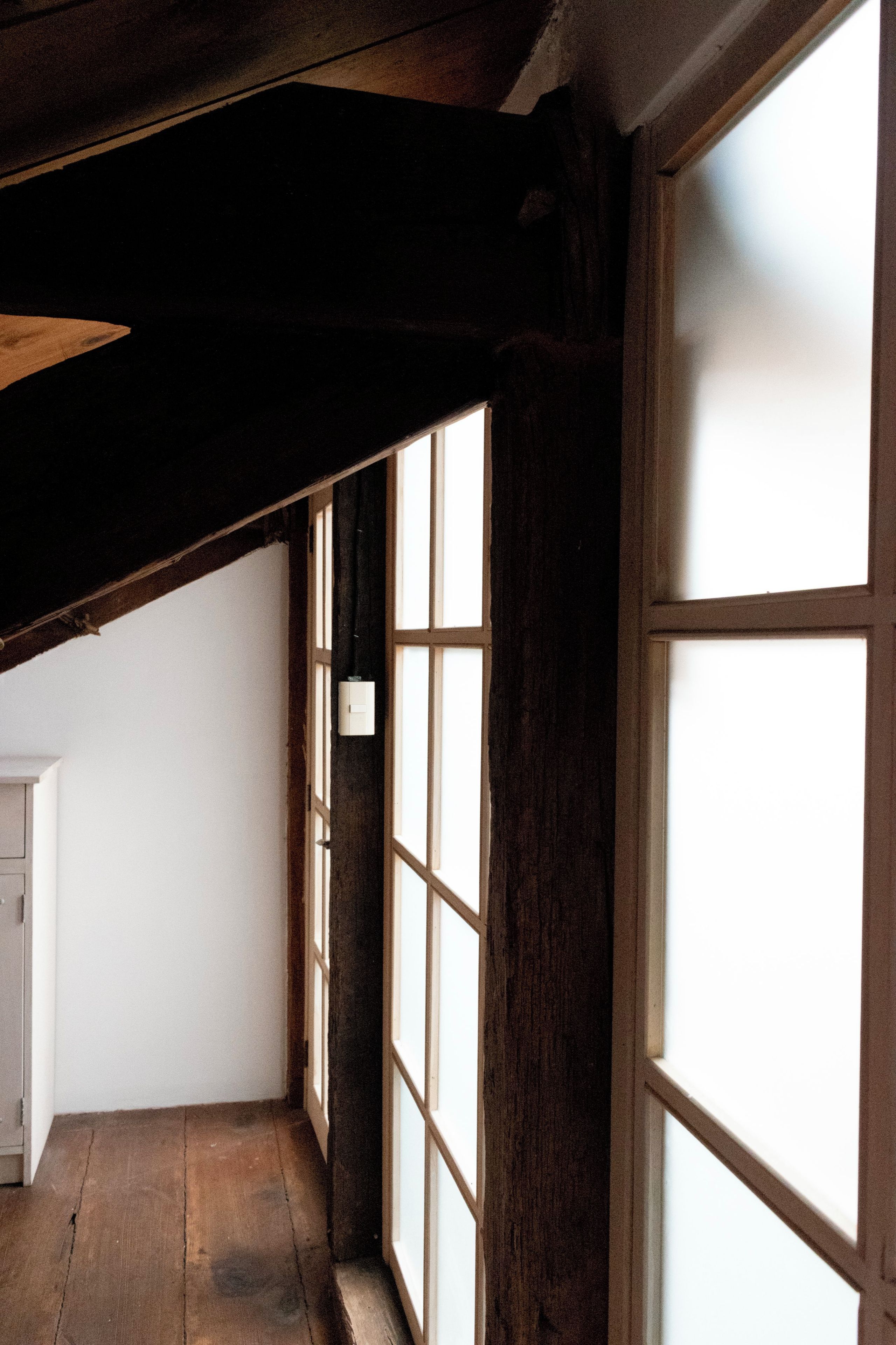 Un couloir étroit avec des poutres en bois et de grandes fenêtres.