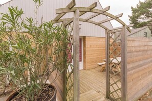 A wooden pergola structure with a lattice design, a potted plant with long leaves, and a wooden deck. - Kargalan Vacation Rental - CRACH - Vacation Rental (CRACH)