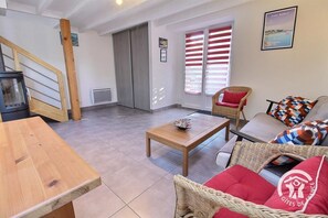 A living room with a wooden table, wicker furniture, a sofa with colorful cushions, and a framed picture on the wall. - Kargalan Vacation Rental - CRACH - Vacation Rental (CRACH)
