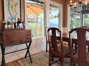 A room with a wooden cabinet, a dining table, chairs, a chandelier, and a window with a view of the outdoors. - Lake Coeur d'Alene 3BR Dock, Kayaks & Boat Slip (Worley)