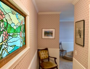 A hallway with a stained glass window, a framed picture on the wall, and a chair. - Lake Coeur d'Alene 3BR Dock, Kayaks & Boat Slip (Worley)
