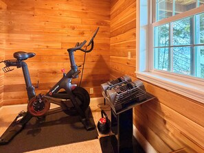 A room with wooden walls, a stationary bike, and a set of dumbbells on a table. - Lake Coeur d'Alene 3BR Dock, Kayaks & Boat Slip (Worley)