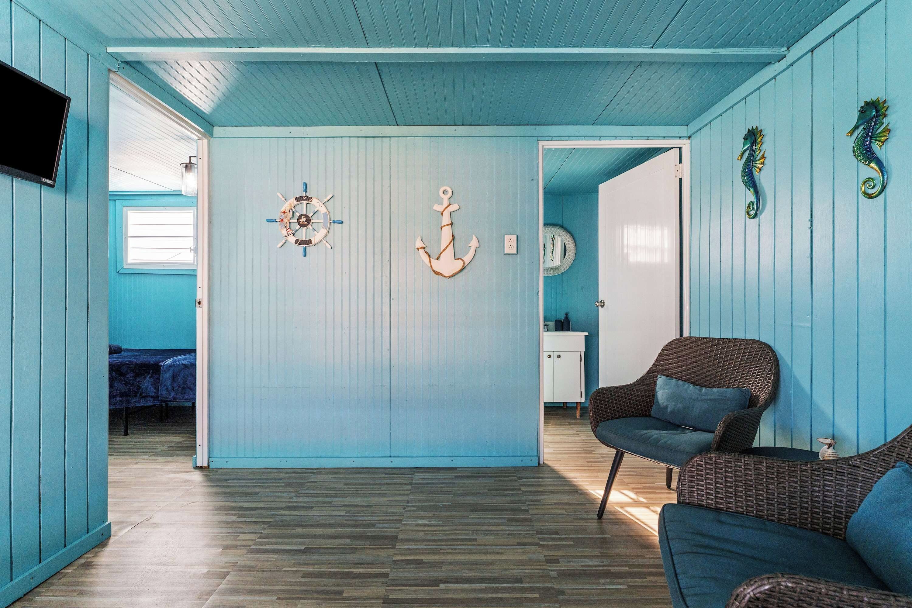 A room with a wooden floor, a bed, a wicker chair, and a wall with nautical decorations.