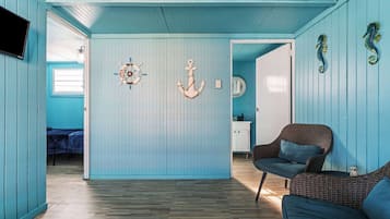 A room with a wooden floor, a bed, a wicker chair, and a wall with nautical decorations.