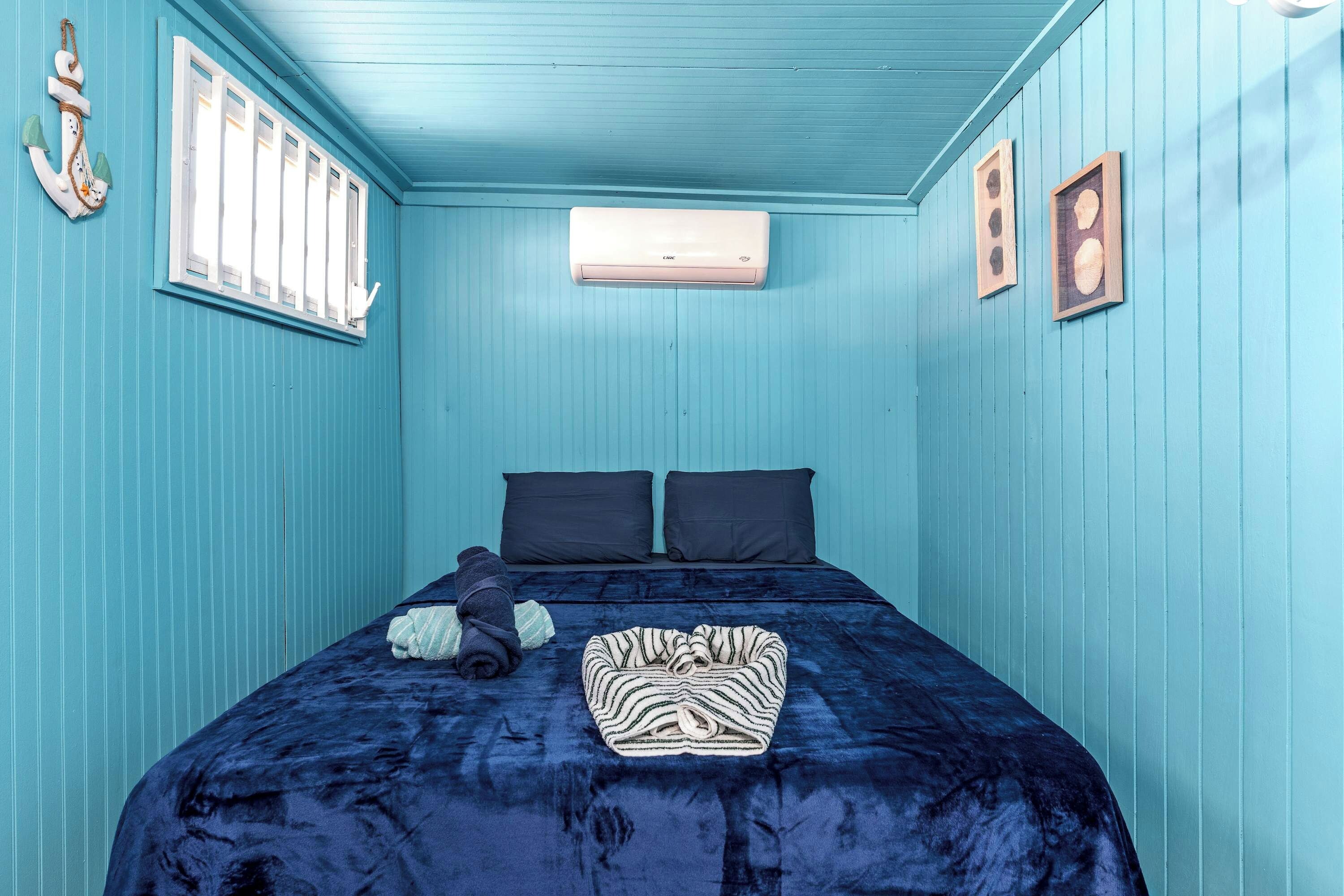 A room with a bed, two pillows, a blanket, and an air conditioning unit.