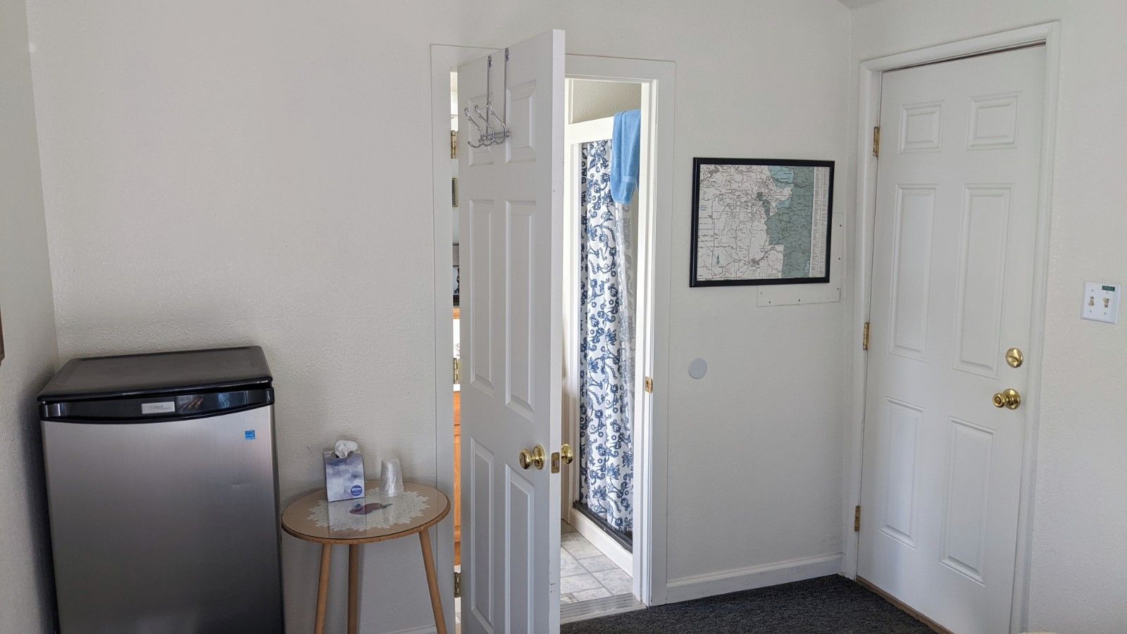 A hallway with a refrigerator, a small table with toiletries, and a door leading to a balcony.