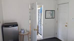 A hallway with a refrigerator, a small table with toiletries, and a door leading to a balcony. - The Apple Place Room #1 (Miramonte)