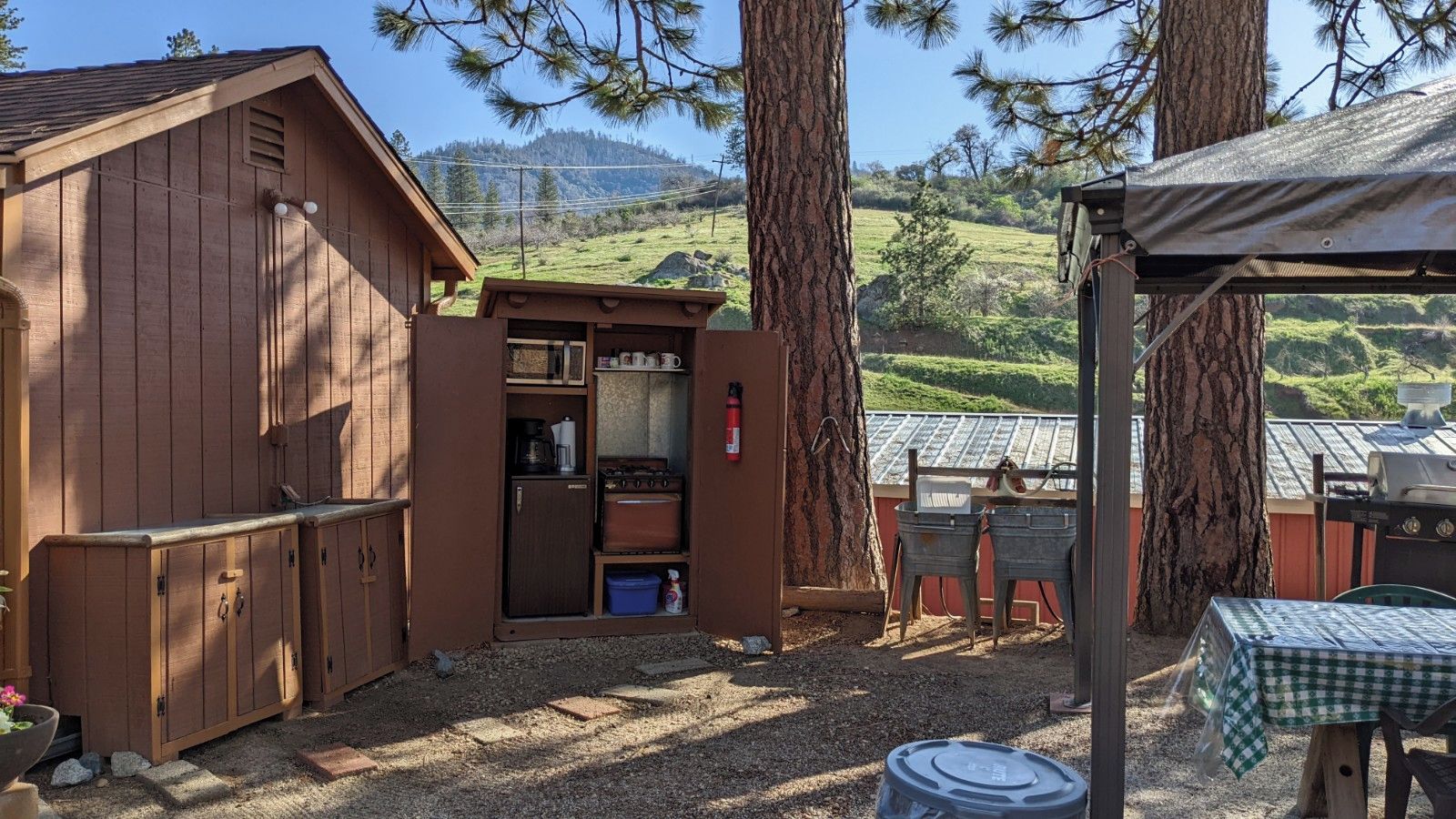 A rustic cabin with a small kitchen area, a dining table, and a barbecue grill.