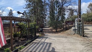 A gated entrance with a wooden pergola and a metal fence, leading to a dirt path. - The Apple Place Room #1 (Miramonte)
