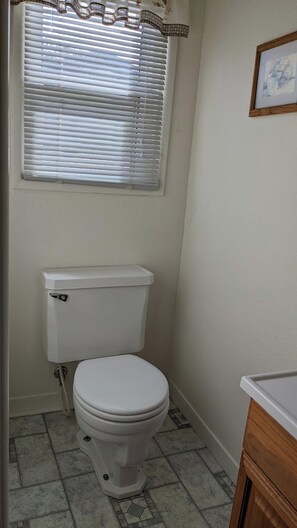 A bathroom with a toilet, a window with blinds, and a framed picture on the wall. - The Apple Place Room #1 (Miramonte)