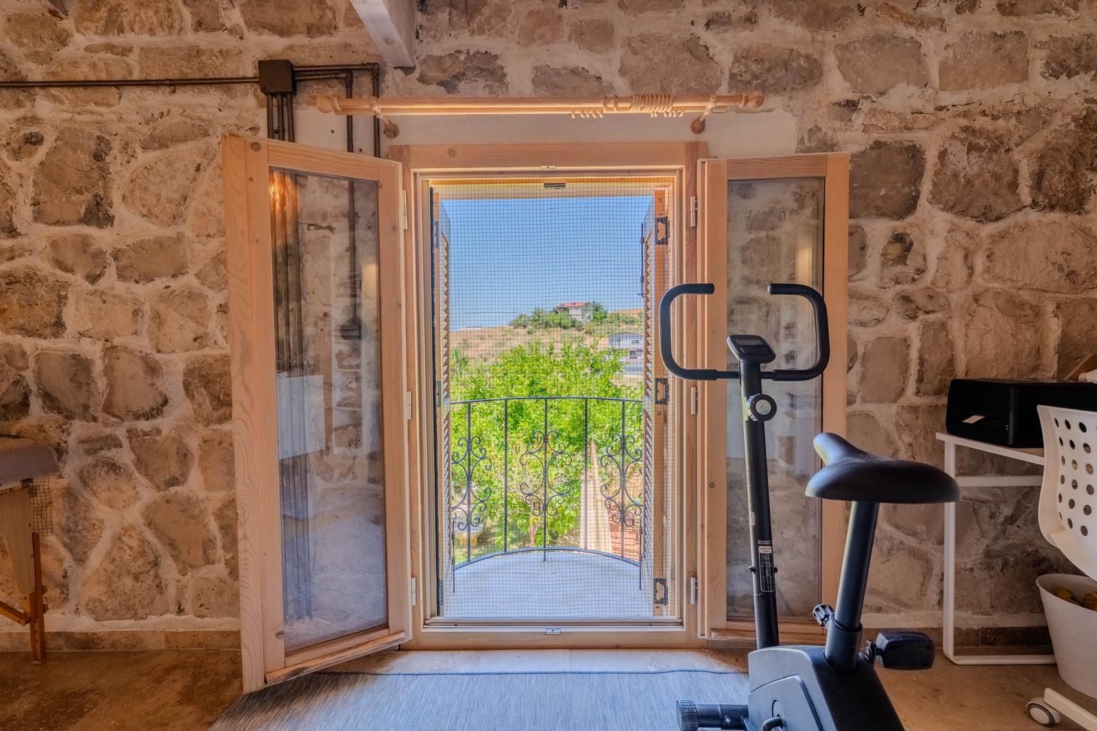 A room with a stone wall, a balcony with a metal railing, and a stationary exercise bike.