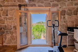 A room with a stone wall, a balcony with a metal railing, and a stationary exercise bike.