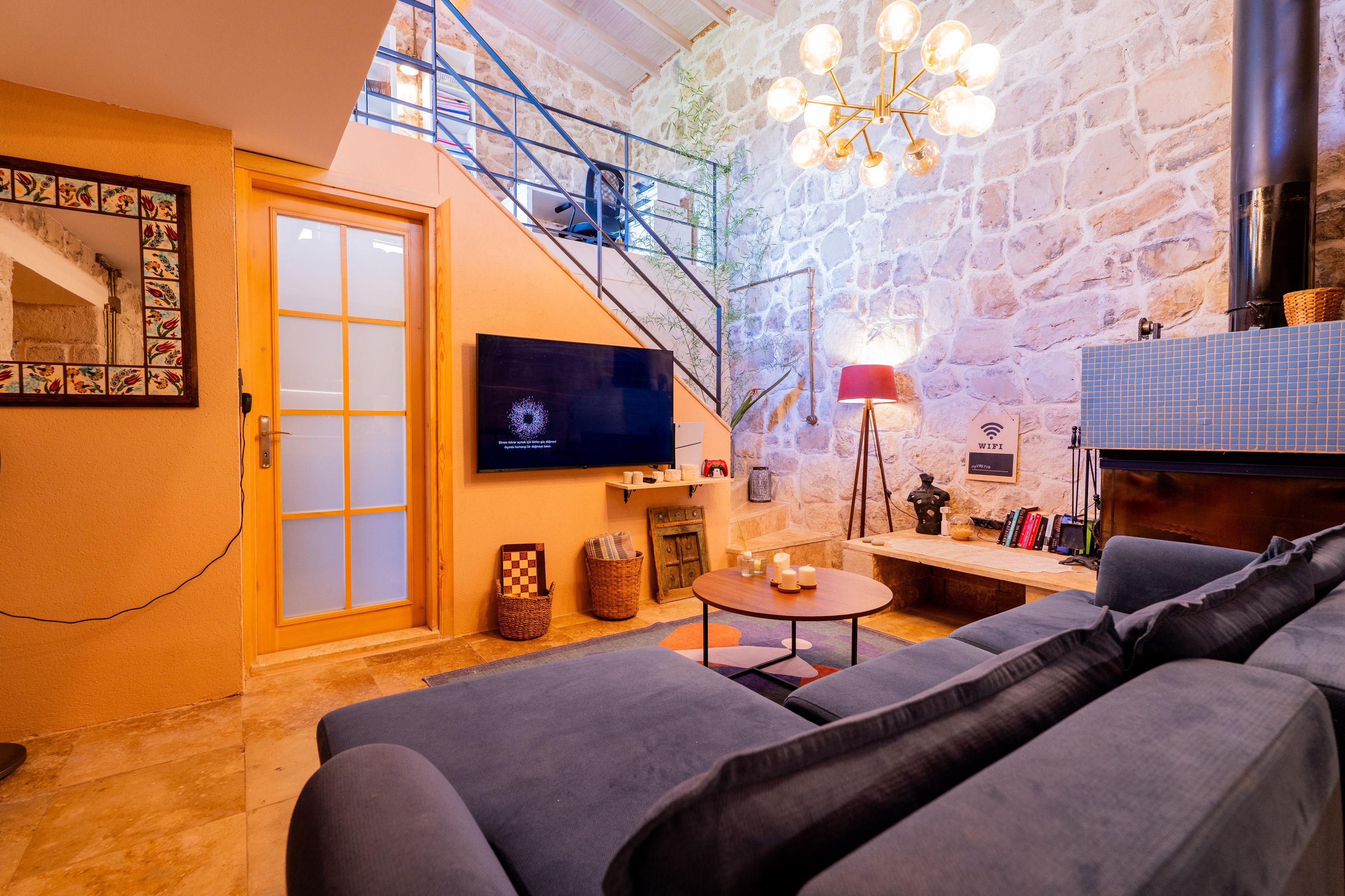 A modern living room with a stone wall, a staircase, a flat-screen TV, a sofa, and a coffee table.