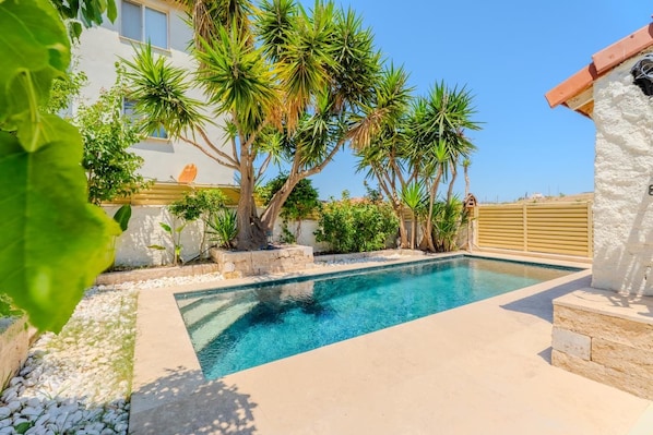 A swimming pool with surrounding vegetation and a building in the background.