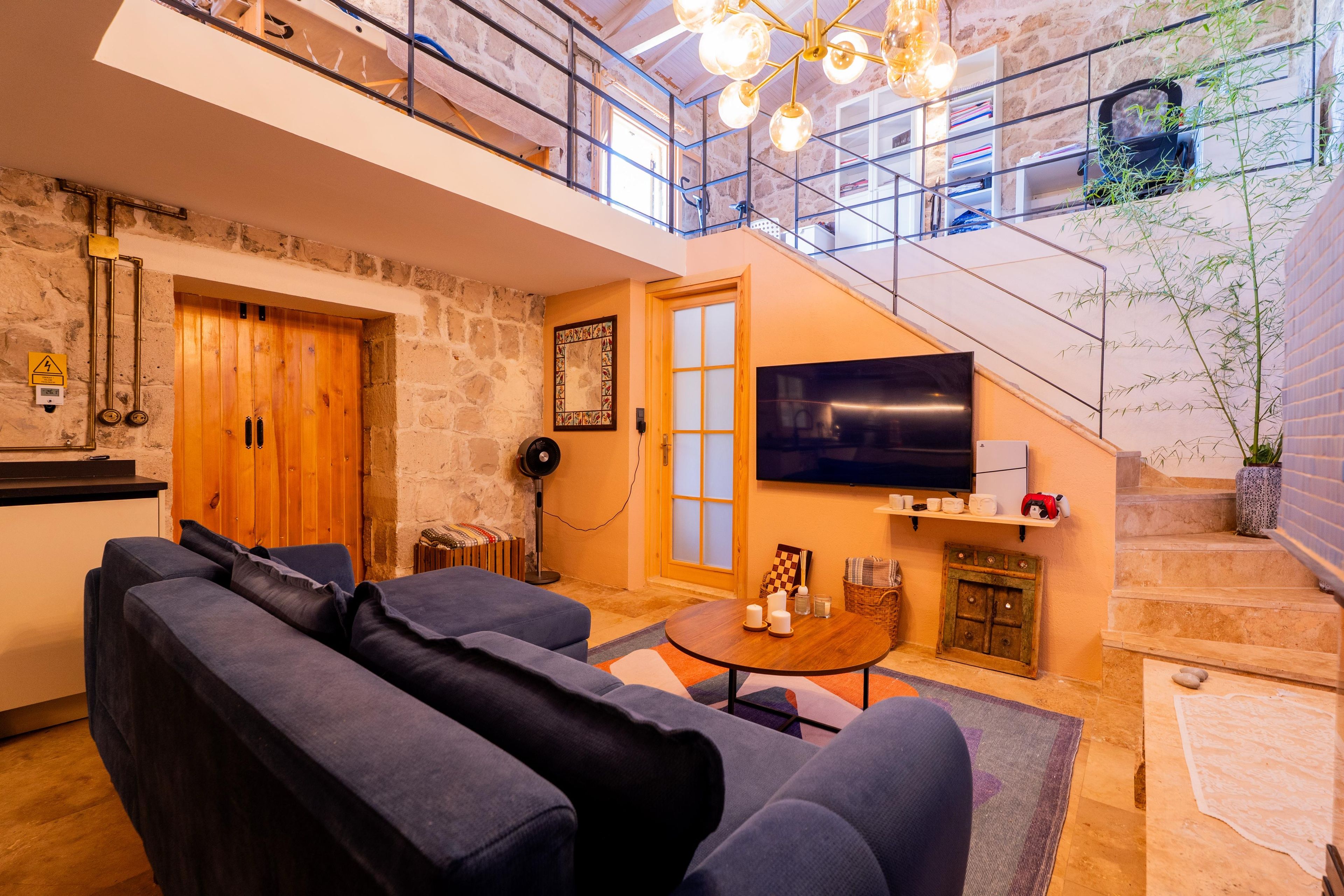 A modern living room with a sofa, a coffee table, and a TV. There is a staircase leading to an upper level.