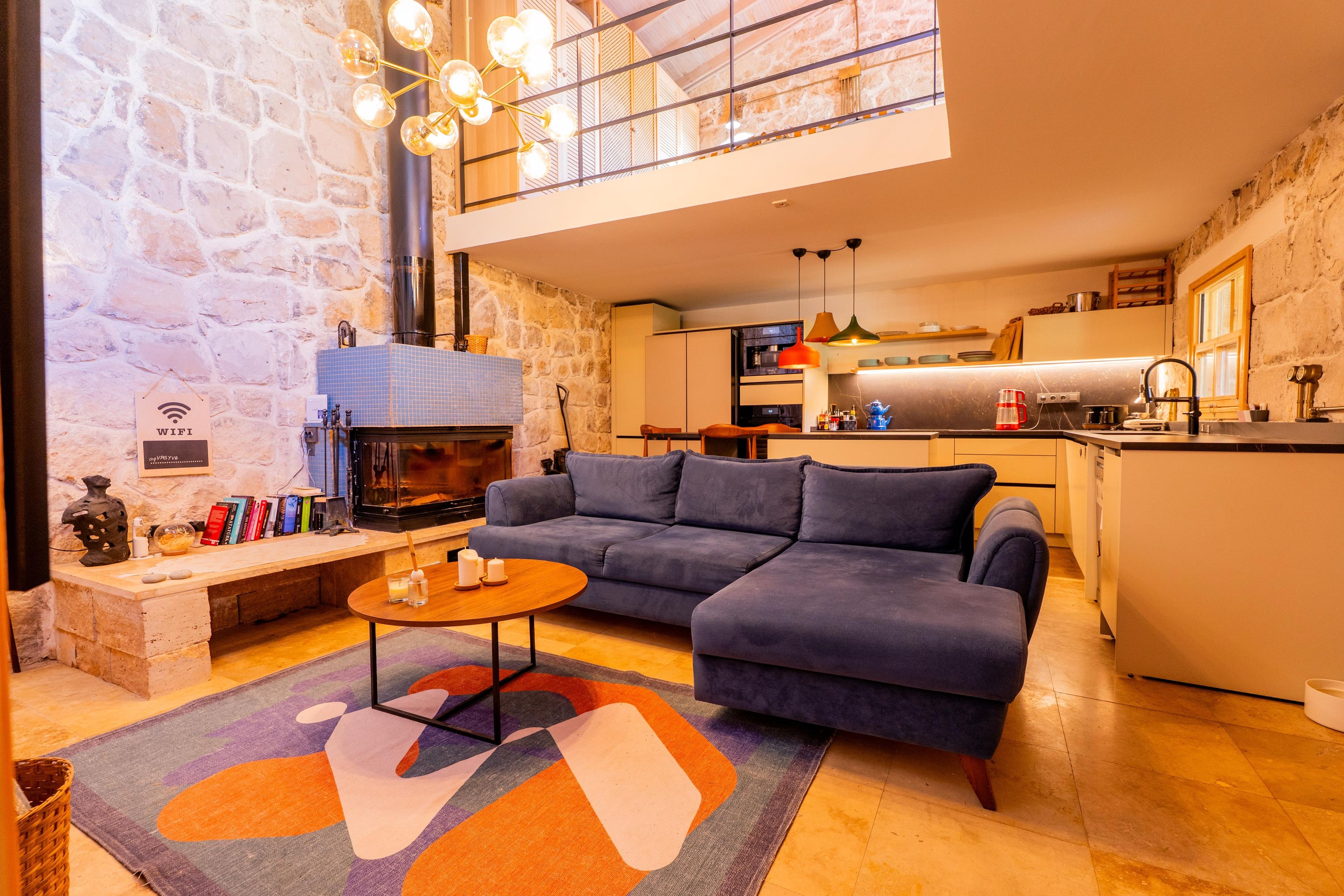 A modern living room with a fireplace, a sofa, a coffee table, and a kitchen in the background.