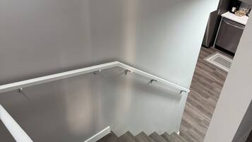 A staircase with a handrail leading to a landing, a kitchen area with appliances, and a wooden floor.