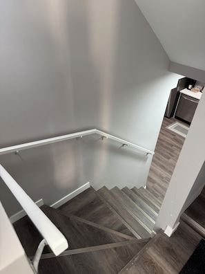Un escalier avec une rampe menant à un palier, un coin cuisine équipé d’appareils électroménagers et un plancher en bois.