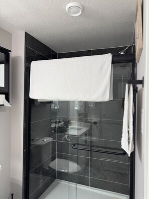 Een moderne badkamer met een glazen douchecabine, een zwart betegelde muur en een witte handdoek aan de douchedeur.
