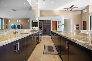 A modern kitchen with dark cabinets, granite countertops, and stainless steel appliances. - Stunning 9 Bedroom Golf Estate - 200 Feet Golf Frontage on Private Course (Rancho Mirage)