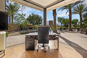 A modern office space with a large desk, chair, and a view of a landscaped garden with palm trees and a pool. - Stunning 9 Bedroom Golf Estate - 200 Feet Golf Frontage on Private Course (Rancho Mirage)