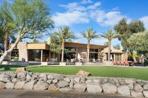 A modern building with a stone facade, large windows, and a patio area with outdoor seating. - Stunning 9 Bedroom Golf Estate - 200 Feet Golf Frontage on Private Course (Rancho Mirage)