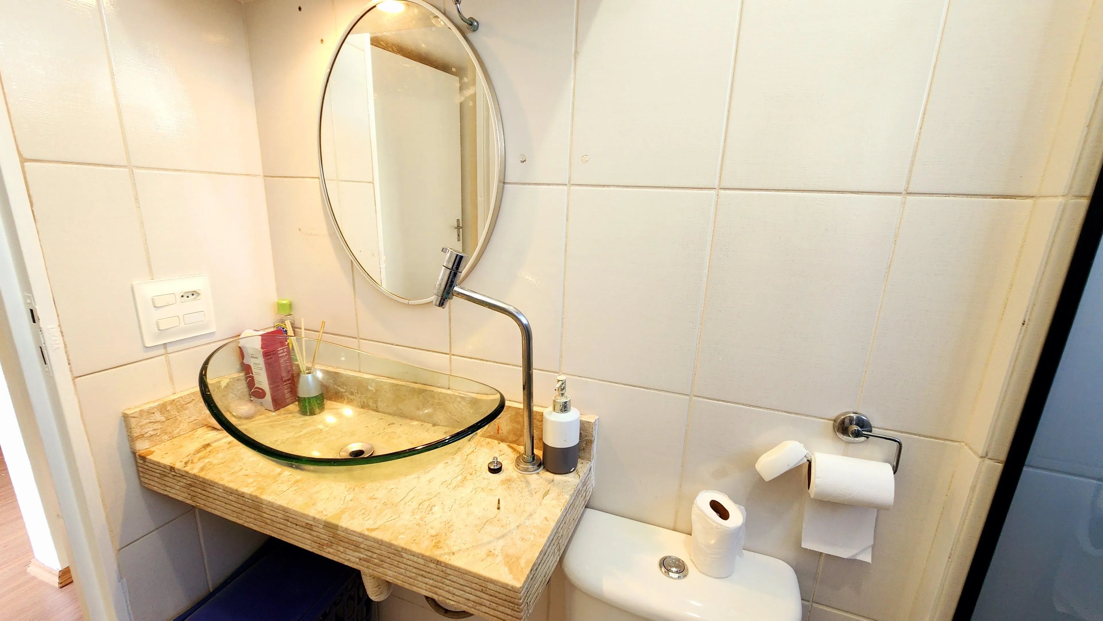 Une salle de bain avec un lavabo en verre, un miroir, des toilettes et un distributeur de serviettes.