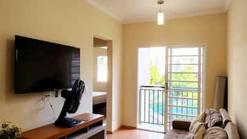 A living room with a flat-screen TV, a wooden entertainment unit, a sofa, and a sliding glass door leading to an outdoor area.