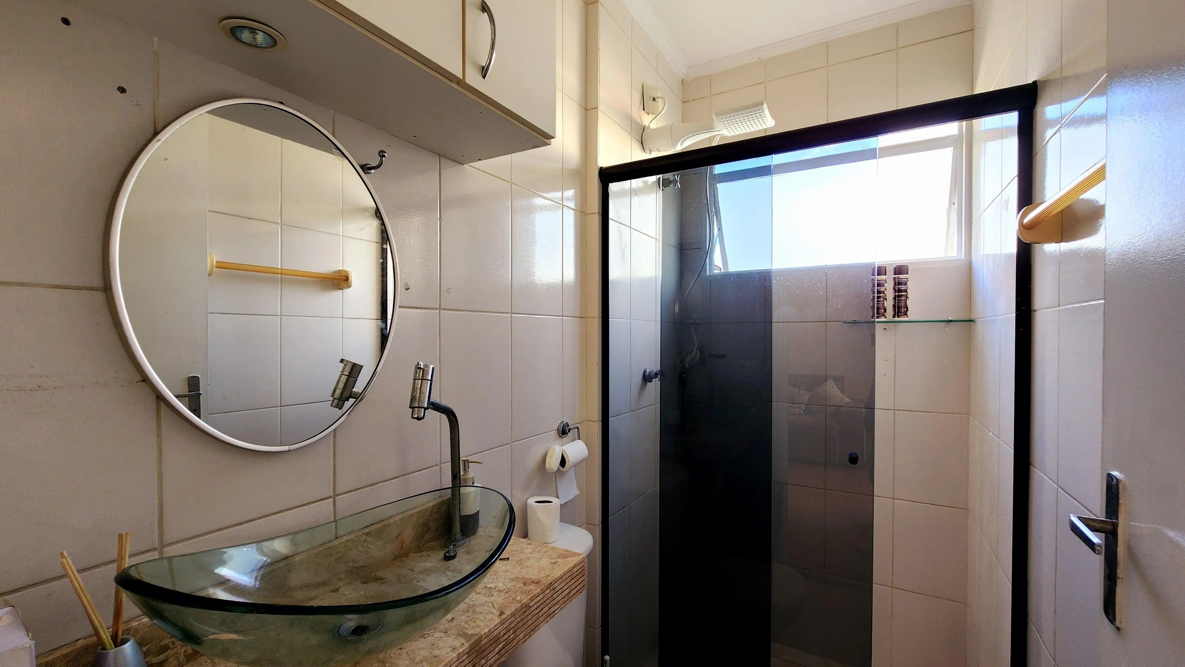 Une salle de bain avec un lavabo en verre, un miroir rond, des toilettes et un espace douche.