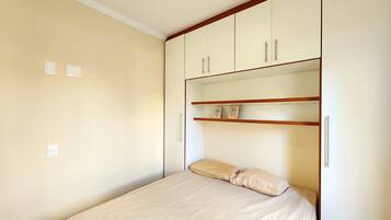 Un dormitorio con cama, un armario de dos puertas y una estantería con dos objetos.