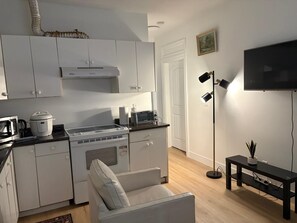 A modern kitchen with white cabinets, a stove, microwave, and a dining area with a white chair.