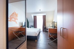 Ein Hotelzimmer mit Bett, Schreibtisch, Stuhl und einem fenster mit Vorhängen.