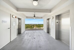 Un corridoio con due ascensori, una ventola a soffitto e vista sulla città da un balcone.