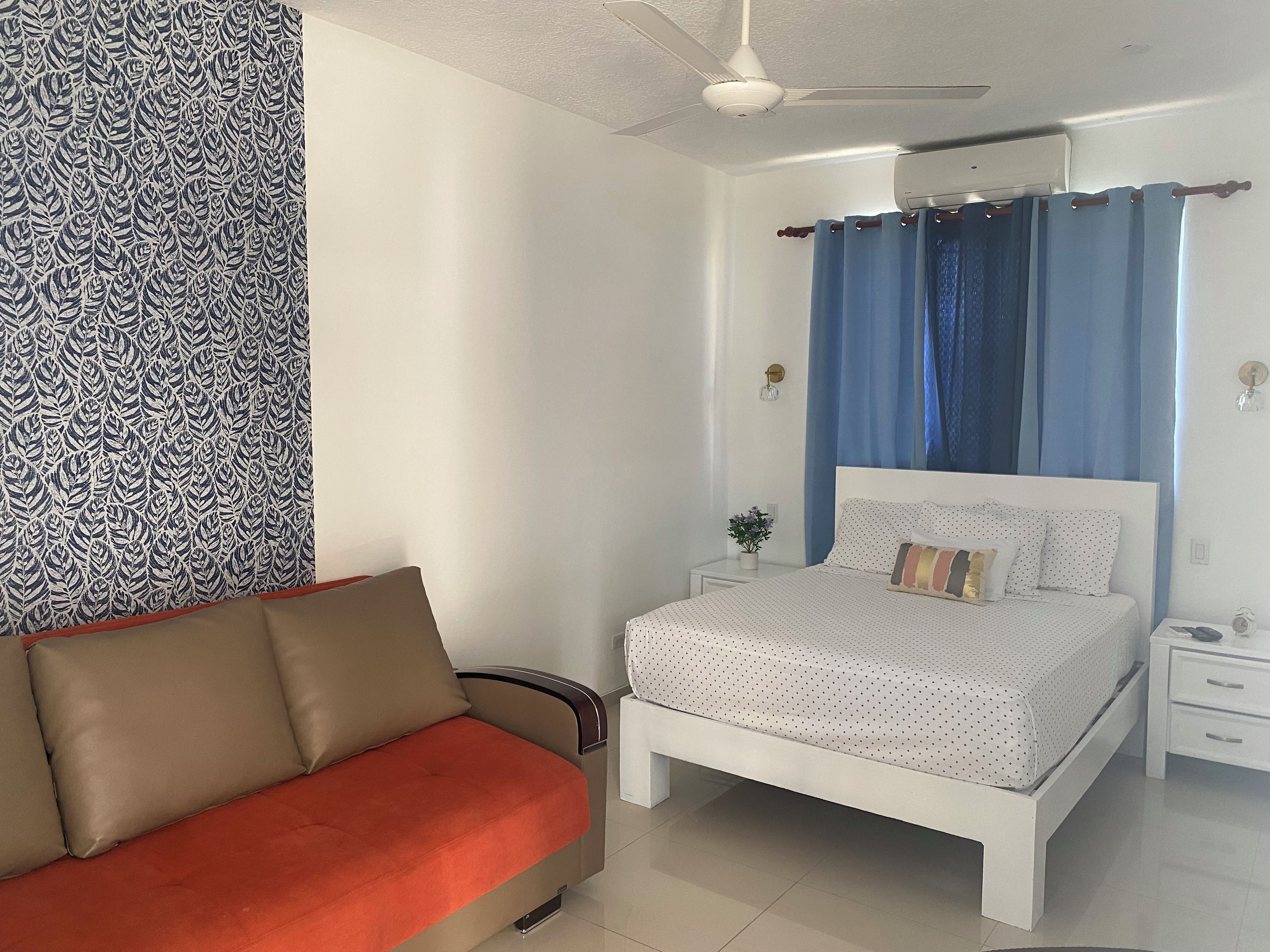Un dormitorio con cama, mesita de noche, luz de pared y ventilador de techo, además de una pared con diseño.