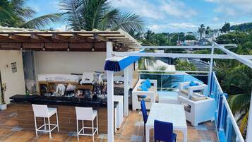 Un bar en la azotea con mesas al aire libre, piscina y vistas a la ciudad.